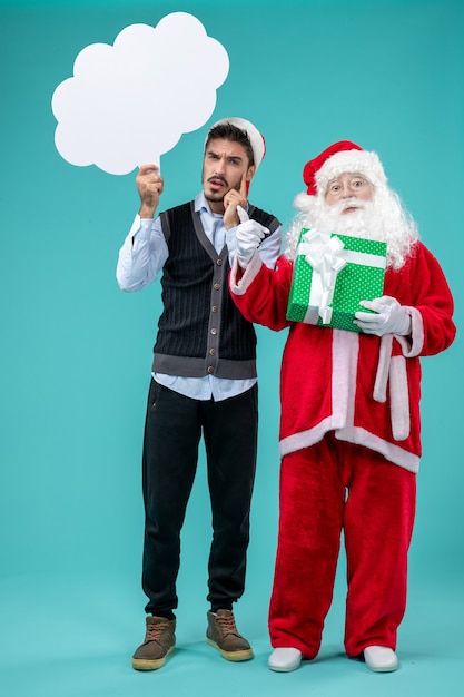 Gratis foto vooraanzicht santa claus met jonge mannelijke whos witte wolk teken op blauwe vloer xmas nieuwjaar vakantie sneeuw houden