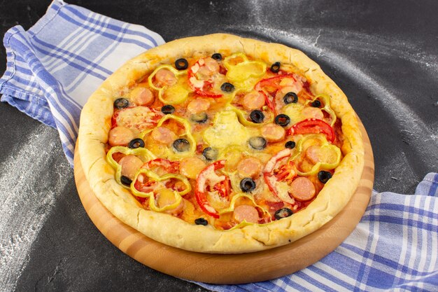Vooraanzicht smakelijke cheesy pizza met rode tomaten, zwarte olijven en worstjes op donker
