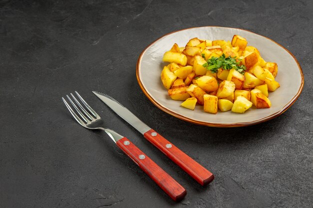 Vooraanzicht smakelijke gebakken aardappelen in bord met greens op de donkere tafel