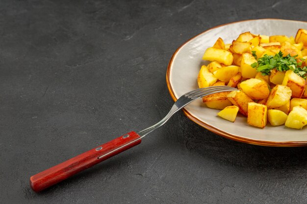 Vooraanzicht smakelijke gebakken aardappelen in bord met greens op de donkere tafel