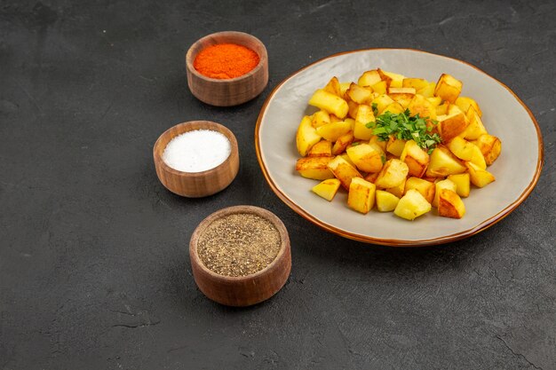 Vooraanzicht smakelijke gebakken aardappelen in bord met kruiden op de donkere tafel