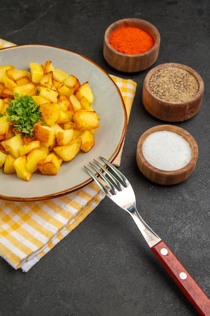 Vooraanzicht smakelijke gebakken aardappelen in bord met kruiden op een donkergrijze tafel