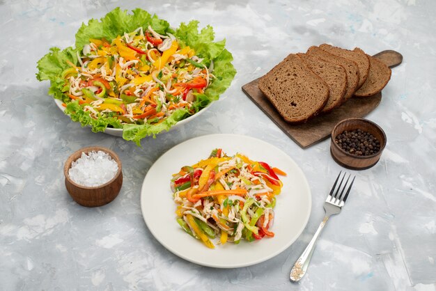 Vooraanzicht smakelijke groente salade met gesneden groenten en groene salade met brood loafs op grijze, plantaardige salade maaltijd