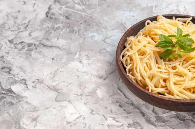 Vooraanzicht smakelijke spaghetti met groen blad op witte tafel maaltijdschotel deeg pasta