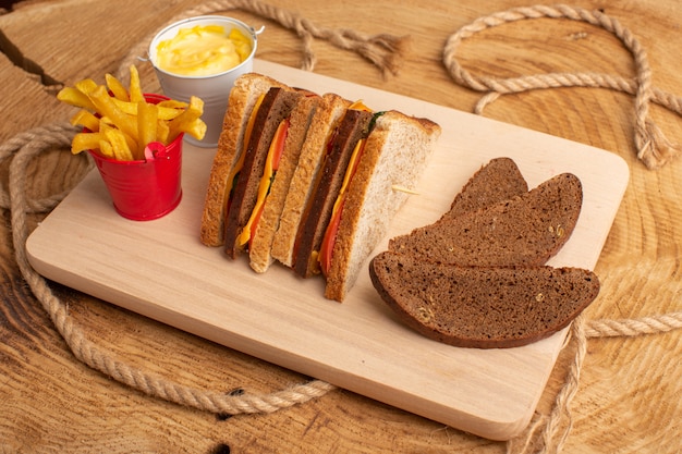 Gratis foto vooraanzicht smakelijke toast sandwich met kaas ham samen met frietjes zure room brood broden op hout