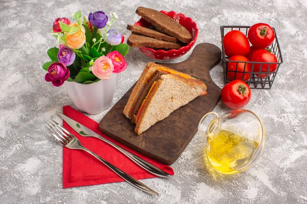 Vooraanzicht smakelijke toastsandwiches met kaasham met olietomaten en bloemen op wit