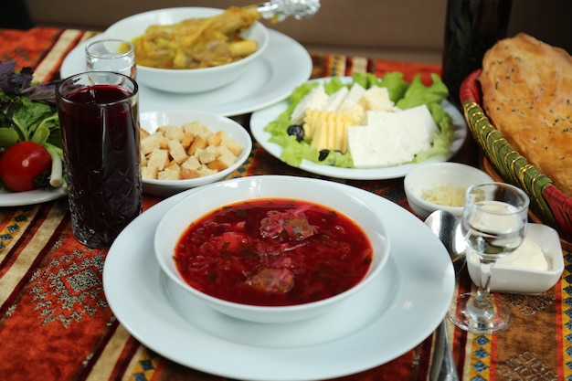 Vooraanzicht traditionele oekraïense schotel borsch in een bord met kaas en tandoor brood met een glas wodka en sap op tafel