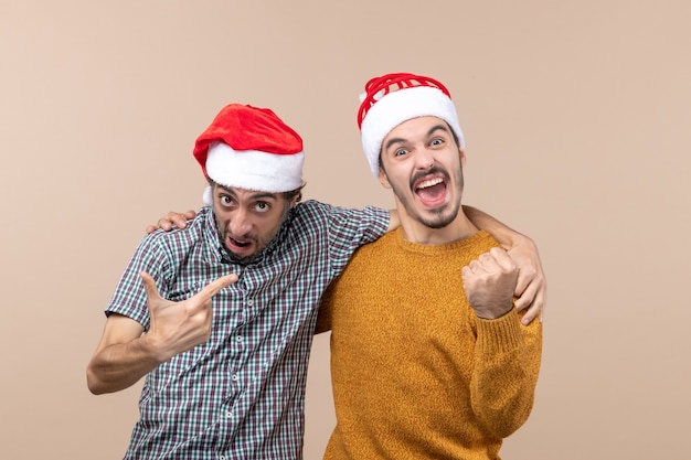 Vooraanzicht twee enthousiaste jongens met santahoeden die elkaar op beige geïsoleerde achtergrond omhelzen