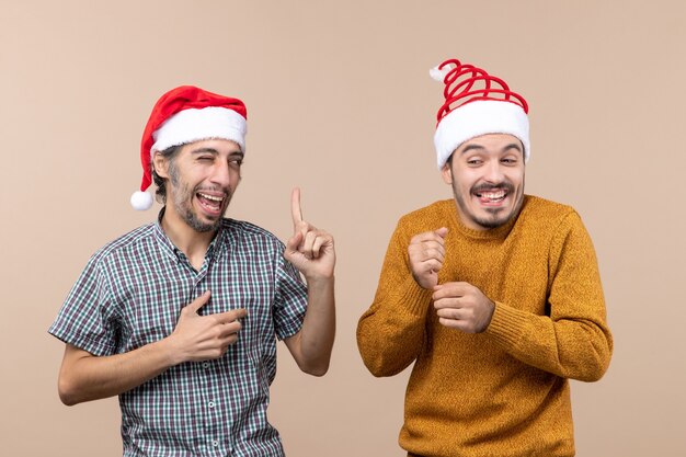 Vooraanzicht twee gelukkige jongens met santahoeden één met knipperend oog op beige geïsoleerde achtergrond