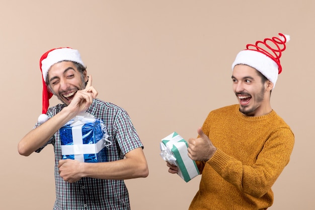Vooraanzicht twee gelukkige jongens praten en houden kerstcadeautjes op beige geïsoleerde achtergrond