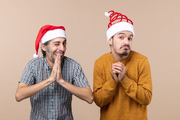 Gratis foto vooraanzicht twee grappige jongens met kerstmutsen één met knipperende ogen op beige geïsoleerde achtergrond