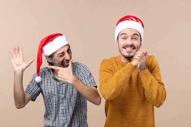 Vooraanzicht twee jongens met santahoeden die zijn hand tonen die andere met gesloten ogen beige geïsoleerde achtergrond wensen