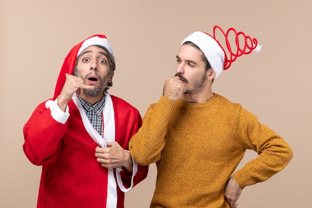 Gratis foto vooraanzicht twee mannen met santahoeden die op beige geïsoleerde achtergrond denken