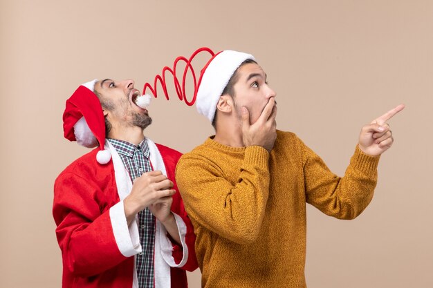 Vooraanzicht twee mannen met santahoeden één die hoedenpompon proberen te vangen en de andere die richting op beige geïsoleerde achtergrond tonen