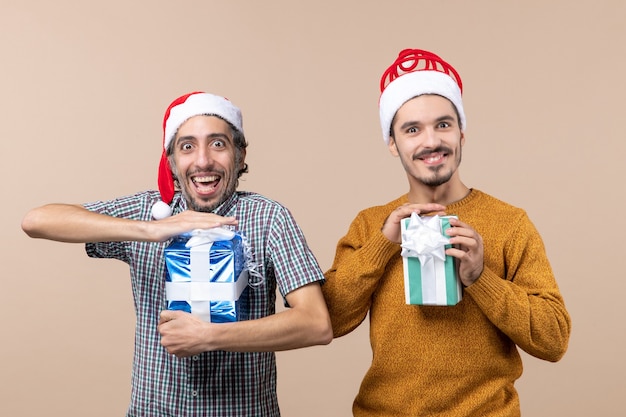 Vooraanzicht twee verwarde jongens genieten van en houden van kerstcadeaus op beige geïsoleerde achtergrond