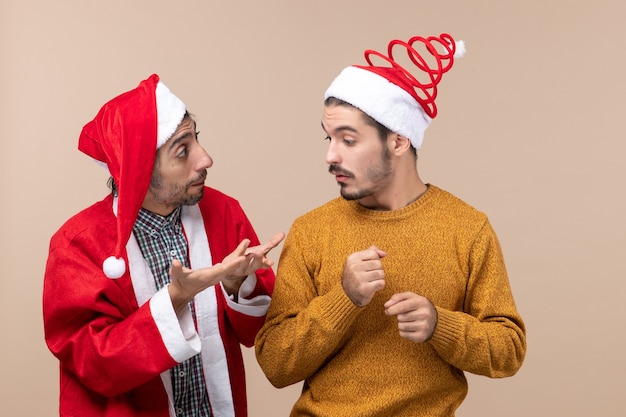 Vooraanzicht twee vrienden met kerstmutsen praten op beige geïsoleerde achtergrond