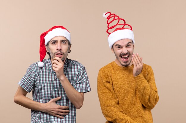 Vooraanzicht twee xmas kerels verward en gelukkig met santahoeden op beige geïsoleerde achtergrond