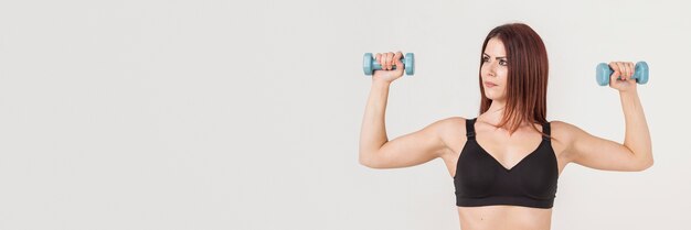 Vooraanzicht van atletische vrouw die gewichten steunt en haar bicepsen toont