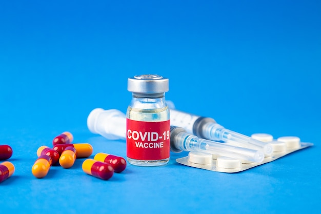 Vooraanzicht van covid-vaccinampullen en capsules verpakte pillen-spuiten op blauwe golfachtergrond