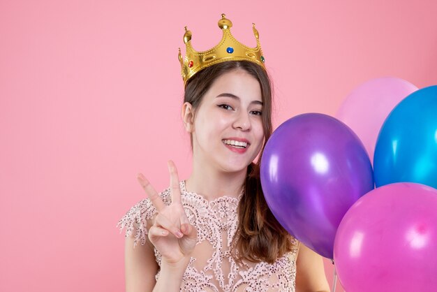 Vooraanzicht van de close-up schattig feest meisje met kroon overwinning teken houden ballonnen maken