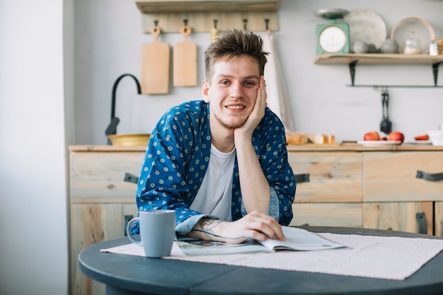 Vooraanzicht van de glimlachende mens die camera met tijdschrift en kop van koffie bekijken