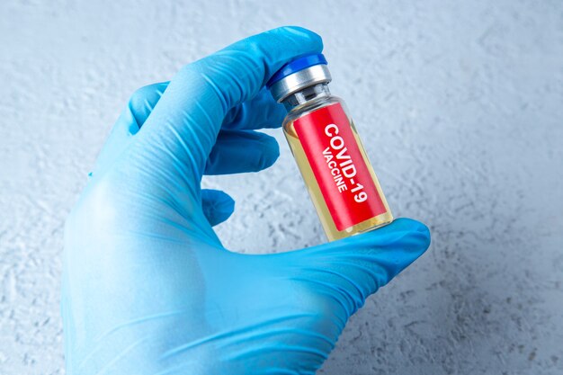 Vooraanzicht van de hand van de arts met covid-vaccinampul op grijze zandachtergrond