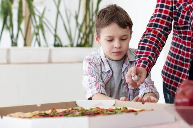 Vooraanzicht van de handen van de moeder ontsmettende zoon alvorens pizza te eten