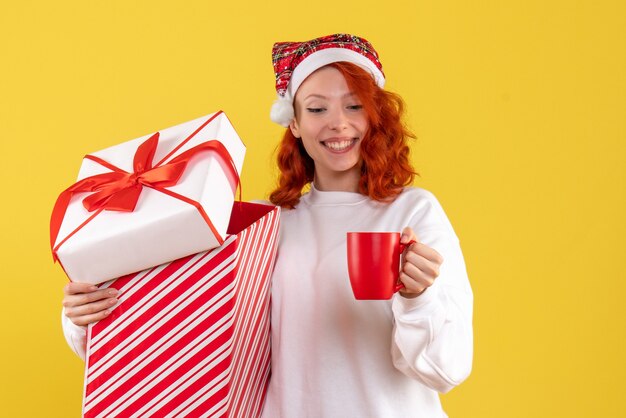 Vooraanzicht van de jonge aanwezige Kerstmis van de vrouwenholding en kopje thee op gele muur