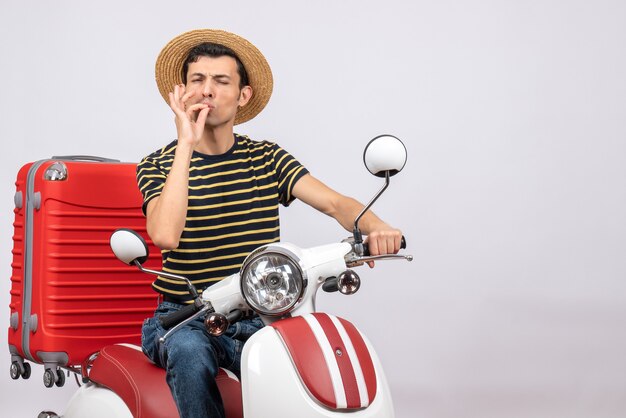 Vooraanzicht van de jonge man die met strohoed op bromfiets smakelijk teken maakt