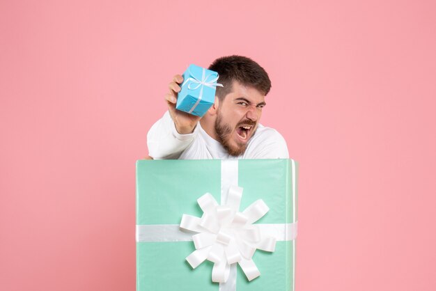 Gratis foto vooraanzicht van de jonge man in de huidige doos met een klein geschenk met geschreeuw op roze muur