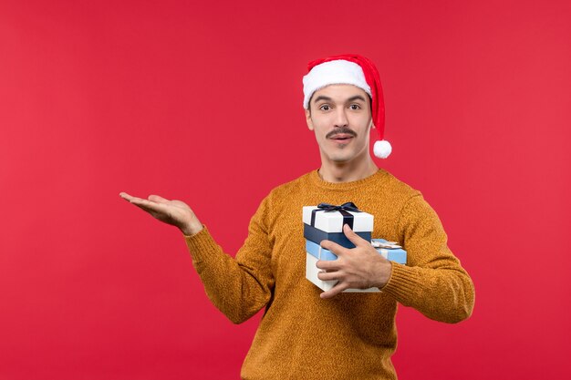 Vooraanzicht van de jonge man met cadeautjes op lichte rode muur