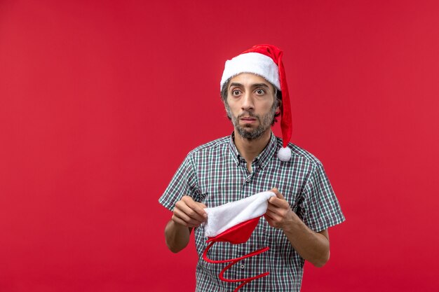 Vooraanzicht van de jonge man met kerst speelgoed pet op de rode muur