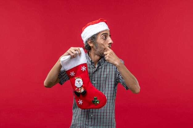 Vooraanzicht van de jonge man met Kerstmissok op rode muur