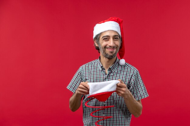 Vooraanzicht van de jonge man met rode kerst speelgoed pet op rode muur