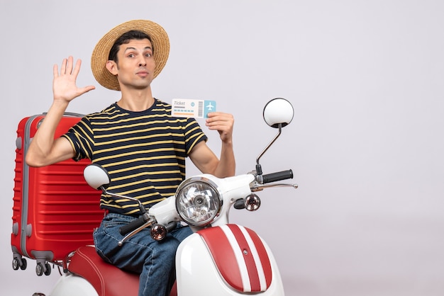 Vooraanzicht van de jonge man met strooien hoed op bromfiets vliegticket zwaaiende hand te houden