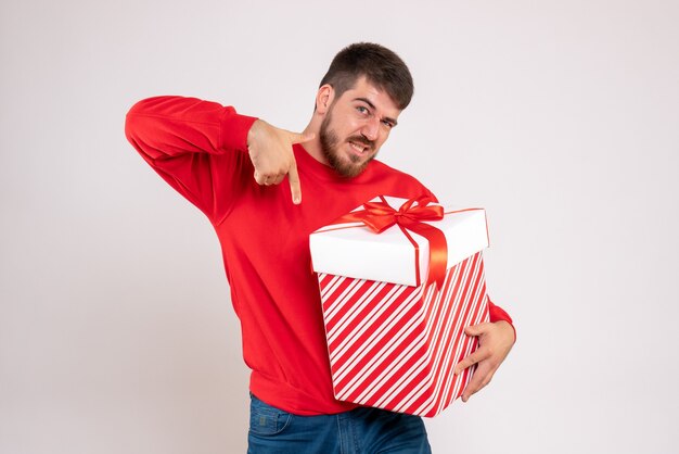 Vooraanzicht van de jonge mens die in rood overhemd Kerstmis in doos op witte muur houdt