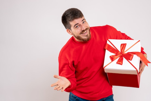 Vooraanzicht van de jonge mens die in rood overhemd kerstmis in doos op witte muur houdt