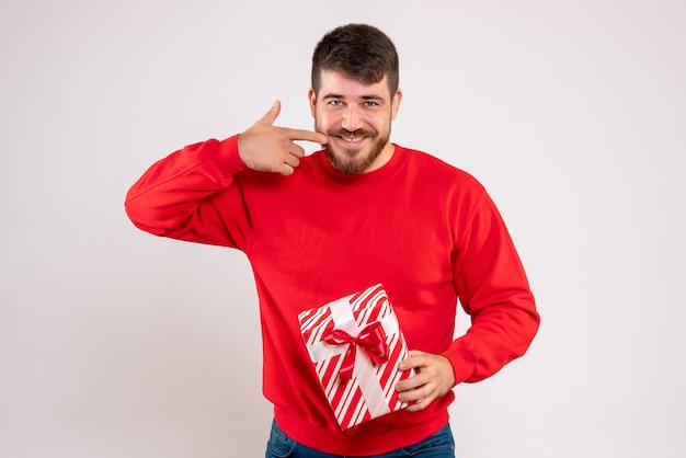 Vooraanzicht van de jonge mens die in rood overhemd Kerstmis op witte muur houdt