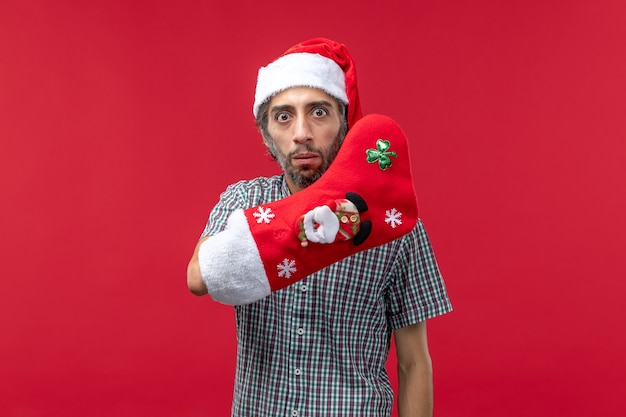 Gratis foto vooraanzicht van de jonge mens die kerstmissok draagt op rode muur