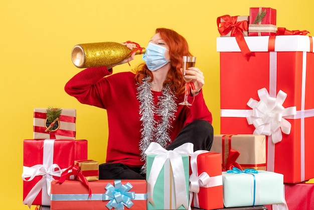 Gratis foto vooraanzicht van de jonge vrouw die rond kerstmis zit presenteert in masker met champagne op gele muur