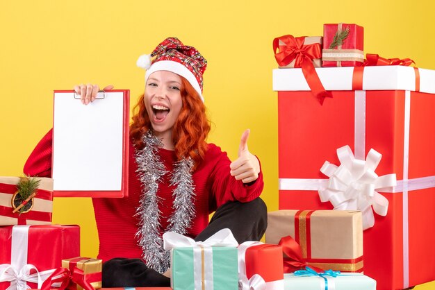 Vooraanzicht van de jonge vrouw die rond kerstmis zit presenteert met dossiernota op gele muur