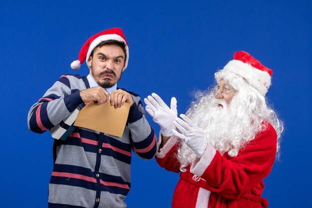 Vooraanzicht van de kerstman met een jonge man die een brief op een blauwe muur scheurt