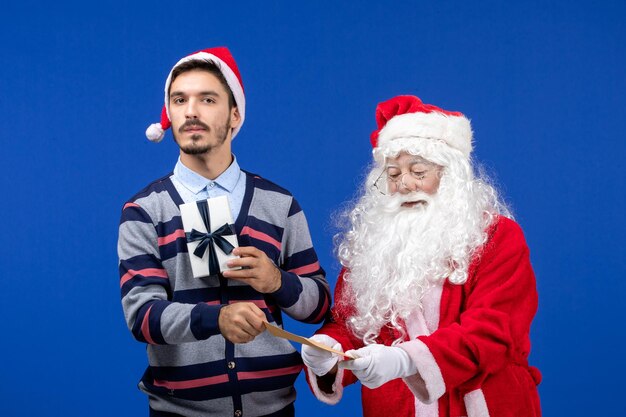 Vooraanzicht van de kerstman met een jonge man die een brief vasthoudt en op de blauwe muur presenteert