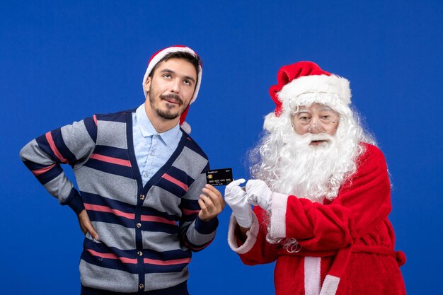 Vooraanzicht van de kerstman met een jonge man met een bankkaart op de blauwe muur