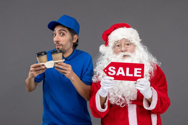 Vooraanzicht van de kerstman met het mannelijke verkoop schrijven van de koeriersholding en koffie op de grijze muur