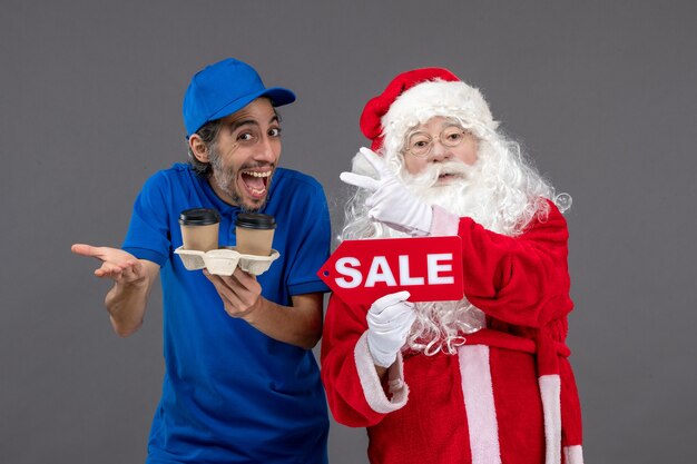 Vooraanzicht van de kerstman met het mannelijke verkoop schrijven van de koeriersholding en koffie op de grijze muur