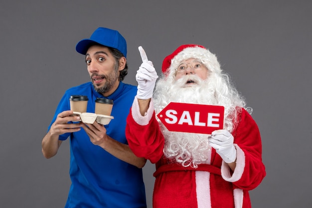 Vooraanzicht van de kerstman met het mannelijke verkoop schrijven van de koeriersholding en koffie op de grijze muur