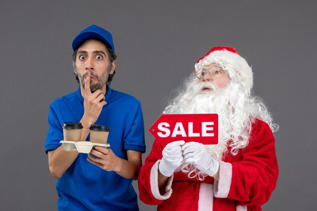 Vooraanzicht van de kerstman met het mannelijke verkoop schrijven van de koeriersholding en koffie op de grijze muur