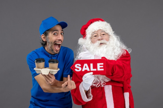 Vooraanzicht van de kerstman met het mannelijke verkoop schrijven van de koeriersholding en koffie op de grijze muur