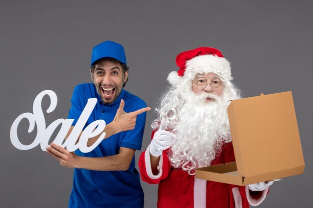 Vooraanzicht van de kerstman met het mannelijke verkoop schrijven van de koeriersholding en lege voedseldoos op de grijze muur